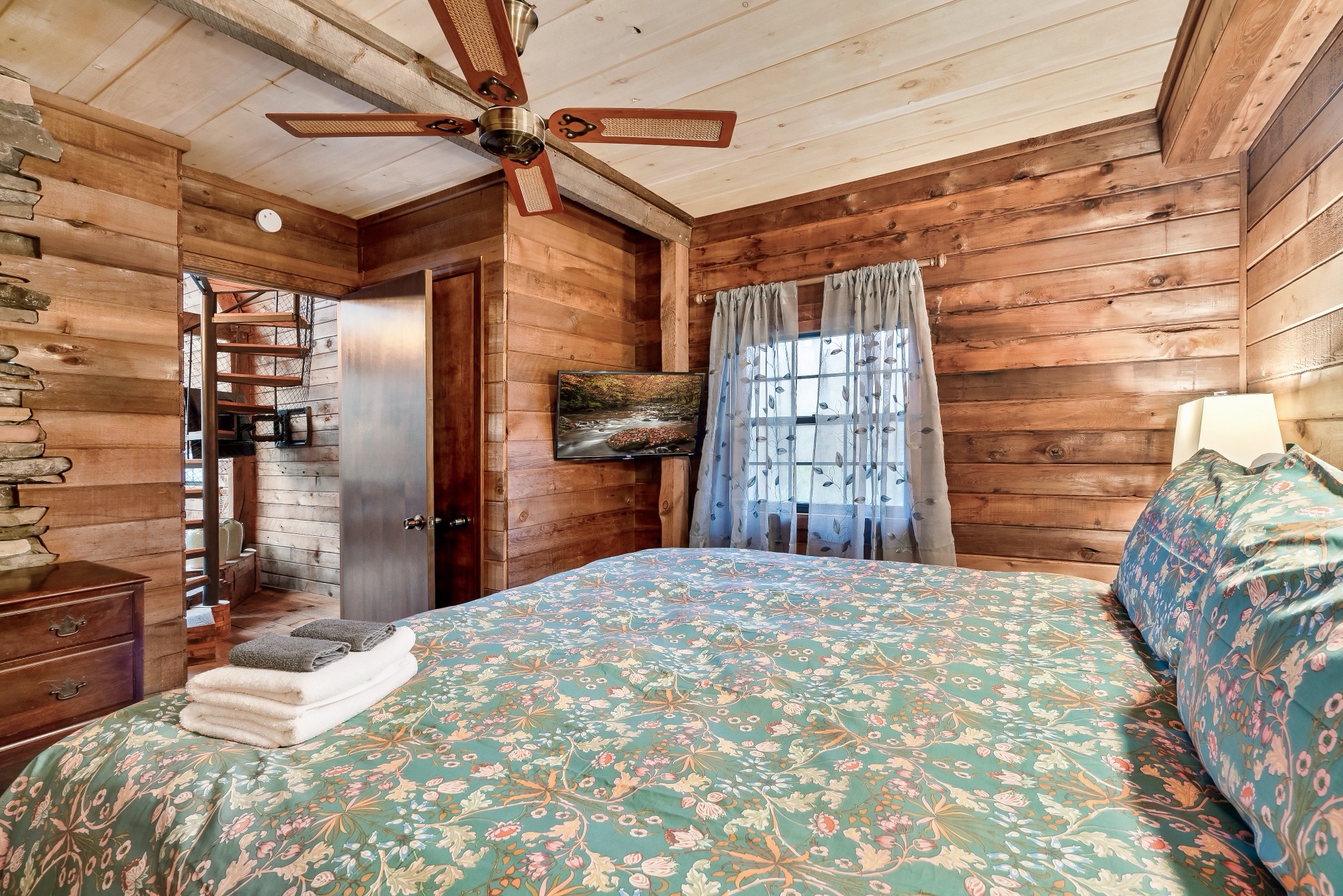 Primary bedroom at Rustic Retreat with a mounted TV and a view toward the spiral staircase